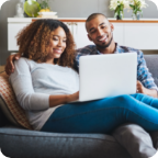 A couple sit together in their home and use a laptop to research insurance online. 